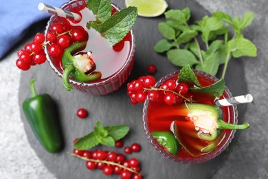 Photo of Glasses of spicy red currant cocktail with jalapeno and mint on grey table, flat lay
