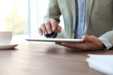 Businessman working with modern tablet at wooden table in office, closeup