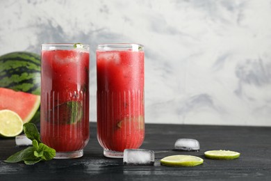Glasses of delicious fresh watermelon juice, lime, mint and ice on black wooden table against textured wall. Space for text