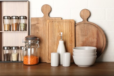 Set of spices and different dishware on wooden table near white brick wall in kitchen