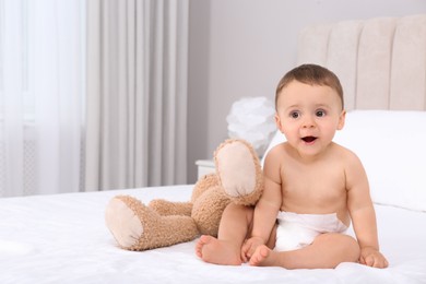 Cute baby in dry soft diaper with toy on white bed at home