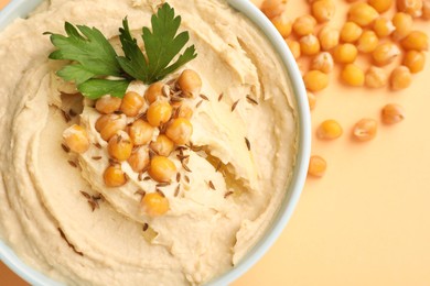 Photo of Bowl of tasty hummus with chickpeas and parsley on beige background, top view