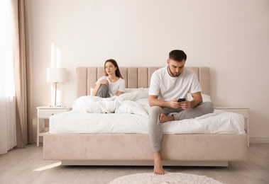 Young man preferring smartphone over his girlfriend on bed at home. Relationship problems