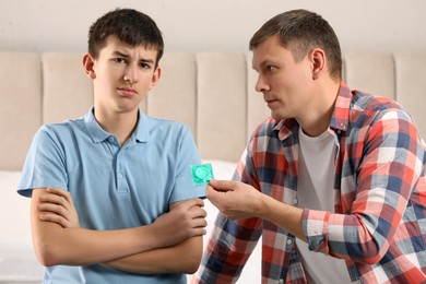 Father giving condom to his teenage son in bedroom. Sex education concept