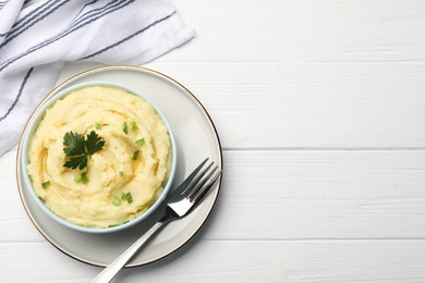 Photo of Bowl of tasty mashed potatoes with parsley and green onion served on white wooden table, top view. Space for text