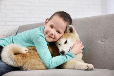 Happy boy with Akita Inu dog on sofa. Little friends