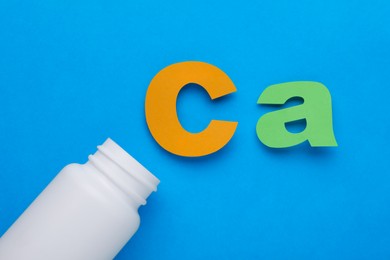 Open bottle and calcium symbol made of colorful letters on light blue background, flat lay