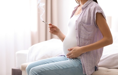 Young pregnant woman smoking cigarette at home, closeup