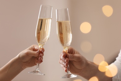 People clinking glasses of champagne against blurred background, closeup. Bokeh effect