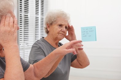 Senior woman looking at reminder note indoors. Age-related memory impairment