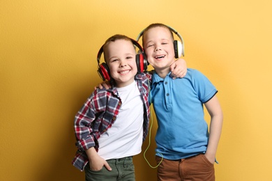Portrait of cute twin brothers with headphones on color background
