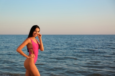 Beautiful young woman in pink stylish swimsuit on beach. Space for text