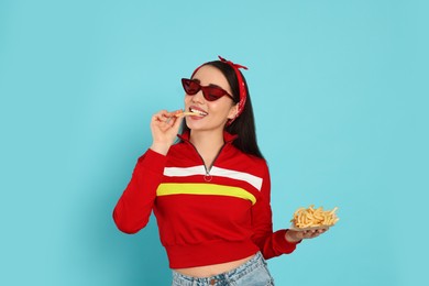 Beautiful young woman eating French fries on light blue background