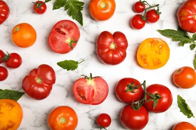 Flat lay composition with different ripe tomatoes and leaves on white marble table