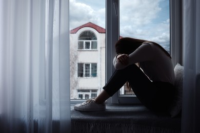 Unhappy young woman crying near window indoors, space for text. Loneliness concept
