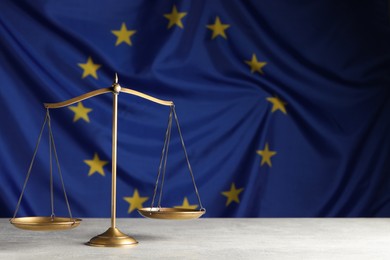 Scales of justice on light grey table against European Union flag. Space for text