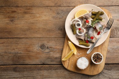 Photo of Salted herring fillets served with thyme, pickles, onion rings, chili pepper and lemon on wooden table, top view. Space for text