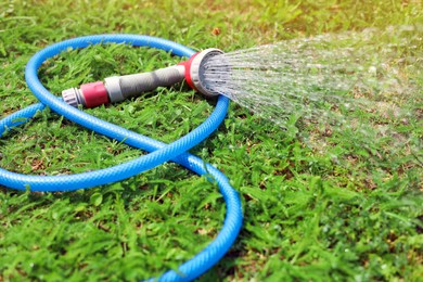 Photo of Water spraying from hose on green grass outdoors