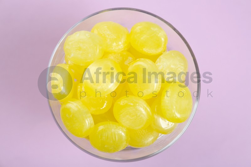 Tasty lemon drops in bowl on violet background, top view