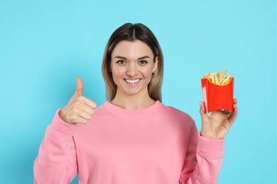 Young woman with French fries on light blue background