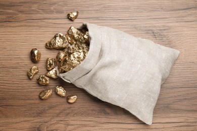 Overturned sack of gold nuggets on wooden table, flat lay