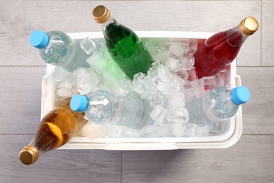 Plastic cool box filled ice cubes and refreshing drinks on wooden floor, top view