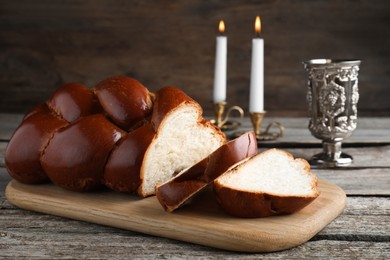 Cut homemade braided bread, goblet and candles on wooden table. Traditional Shabbat challah