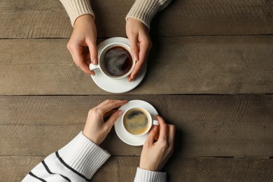 Photo of Women with cups of aromatic coffee at wooden table, top view. Space for text