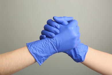 People in medical gloves shaking hands on grey background, closeup