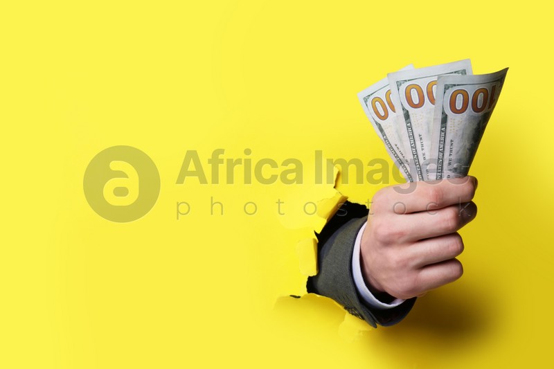 Photo of Businessman breaking through yellow paper with money in fist, closeup. Space for text