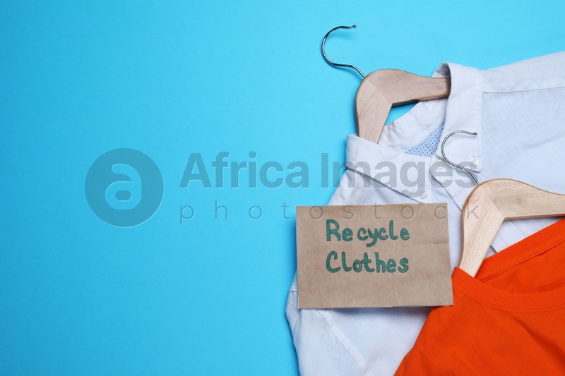 Photo of Different clothes with recycling label and hangers on light blue background, flat lay. Space for text