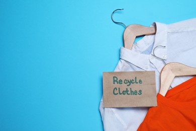 Different clothes with recycling label and hangers on light blue background, flat lay. Space for text