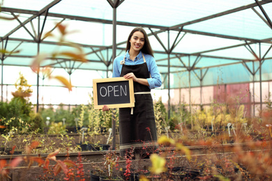 Photo of Female business owner holding OPEN sign in greenhouse