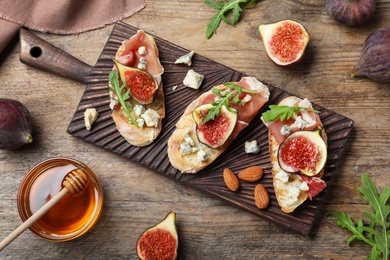 Sandwiches with ripe figs and prosciutto served on wooden table, flat lay
