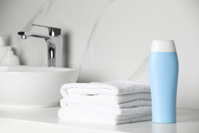 Bottle of shampoo and stacked towels near sink on bathroom counter, space for text