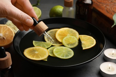 Photo of Woman dripping essential oil into bowl with lemons at grey table, closeup. Aromatherapy treatment
