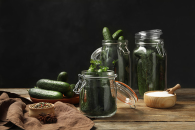 Pickling jars with fresh ripe cucumbers and spices on wooden table