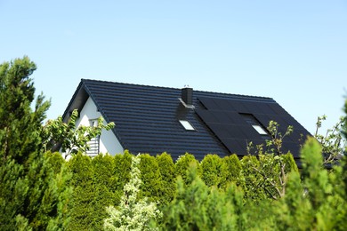 Modern house with black roof and green trees outdoors on sunny day