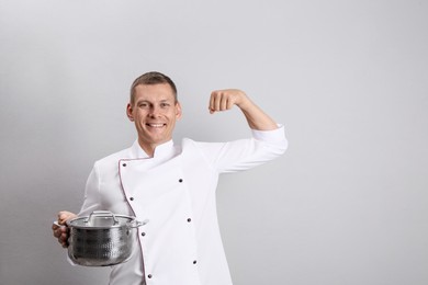 Happy male chef with cooking pot on light grey background. Space for text