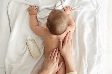 Mother massaging her baby with oil on towel after bathing, top view