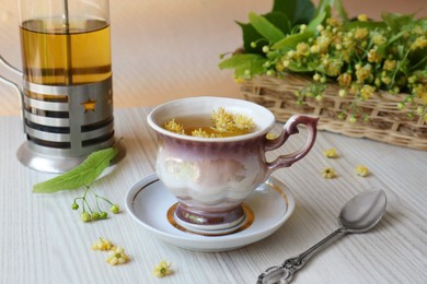 Aromatic tea with linden blossoms and spoon on white wooden table