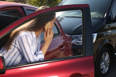 Young woman talking on phone after car accident outdoors
