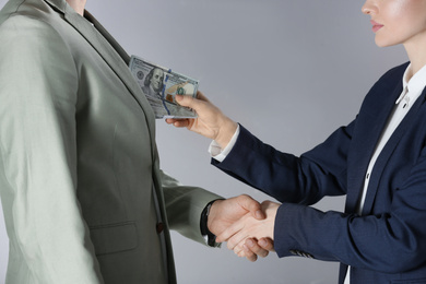 Woman shaking hands with man and offering bribe on grey background, closeup