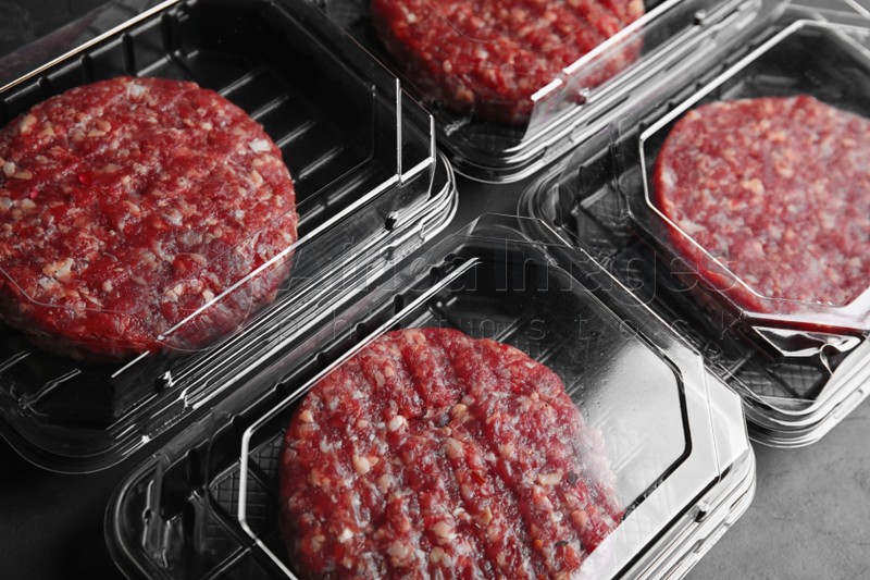 Plastic containers with raw meat cutlets for burger on table, closeup