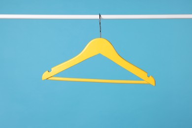 Yellow clothes hanger on metal rail against light blue background