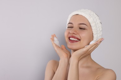 Photo of Young woman washing face with cleansing foam on light grey background, space for text. Skin care cosmetic