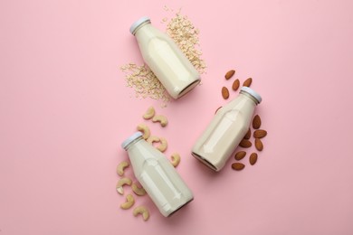 Different vegan milks, oat flakes and nuts on pink background, flat lay