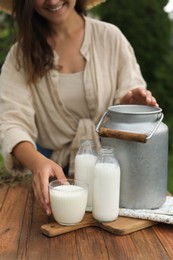 Photo of Smiling woman taking glass with fresh milk at wooden table outdoors, closeup