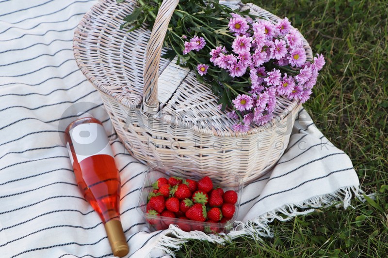 Photo of Picnic basket, flowers, bottle of wine and strawberries on blanket outdoors