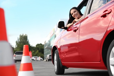 Photo of Young woman in car near traffic cones outdoors. Driving school exam